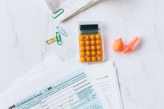 Formulários fiscais e uma calculadora organizados sobre uma mesa de escritório.