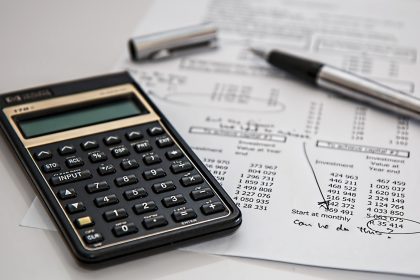 Calculadora, caneta e documentos sobre uma mesa, em contexto de finanças, impostos e contabilidade