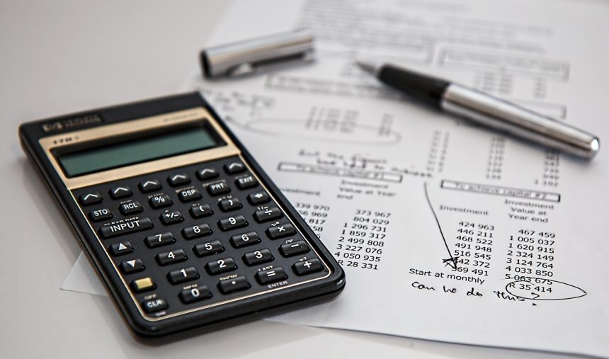 Calculadora, caneta e documentos sobre uma mesa, em contexto de finanças, impostos e contabilidade