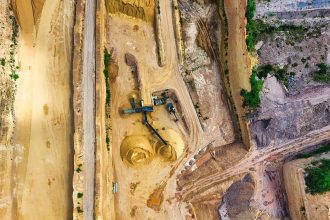 Vista aérea de uma mina a céu aberto, com máquinas e vias de operação cercadas pela paisagem.