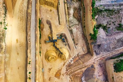 Vista aérea de uma mina a céu aberto, com máquinas e vias de operação cercadas pela paisagem.