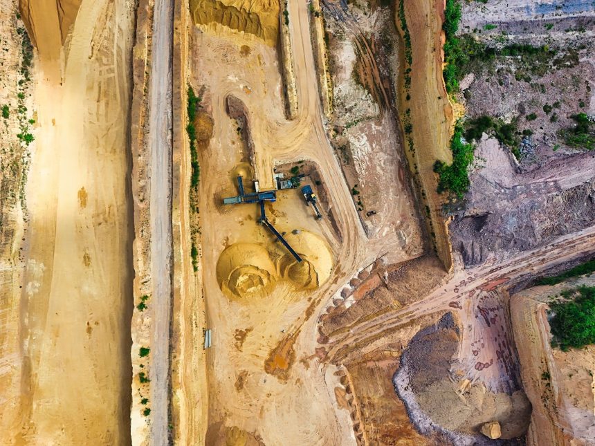 Vista aérea de uma mina a céu aberto, com máquinas e vias de operação cercadas pela paisagem.